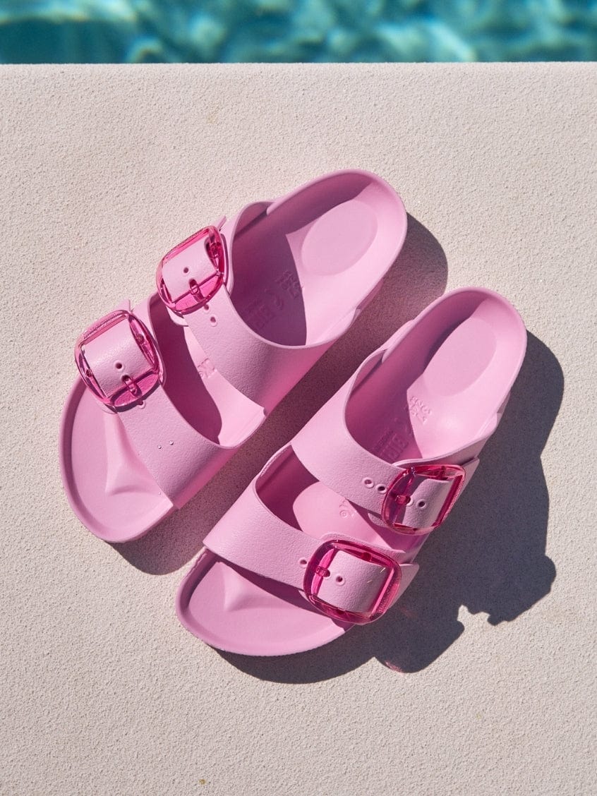 Pink sandals with buckles on a light surface near a pool.