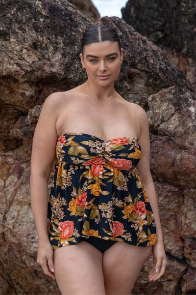 Model standing in front of rocks wearing a black floral strapless tankini top