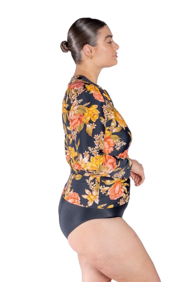 Brunette plus size model wearing zip front long sleeve rash vest in colourful floral print