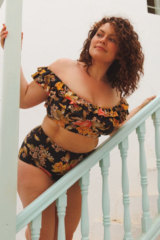 model standing on a stair case in a black floral printed bikini with orange and yellow flowers
