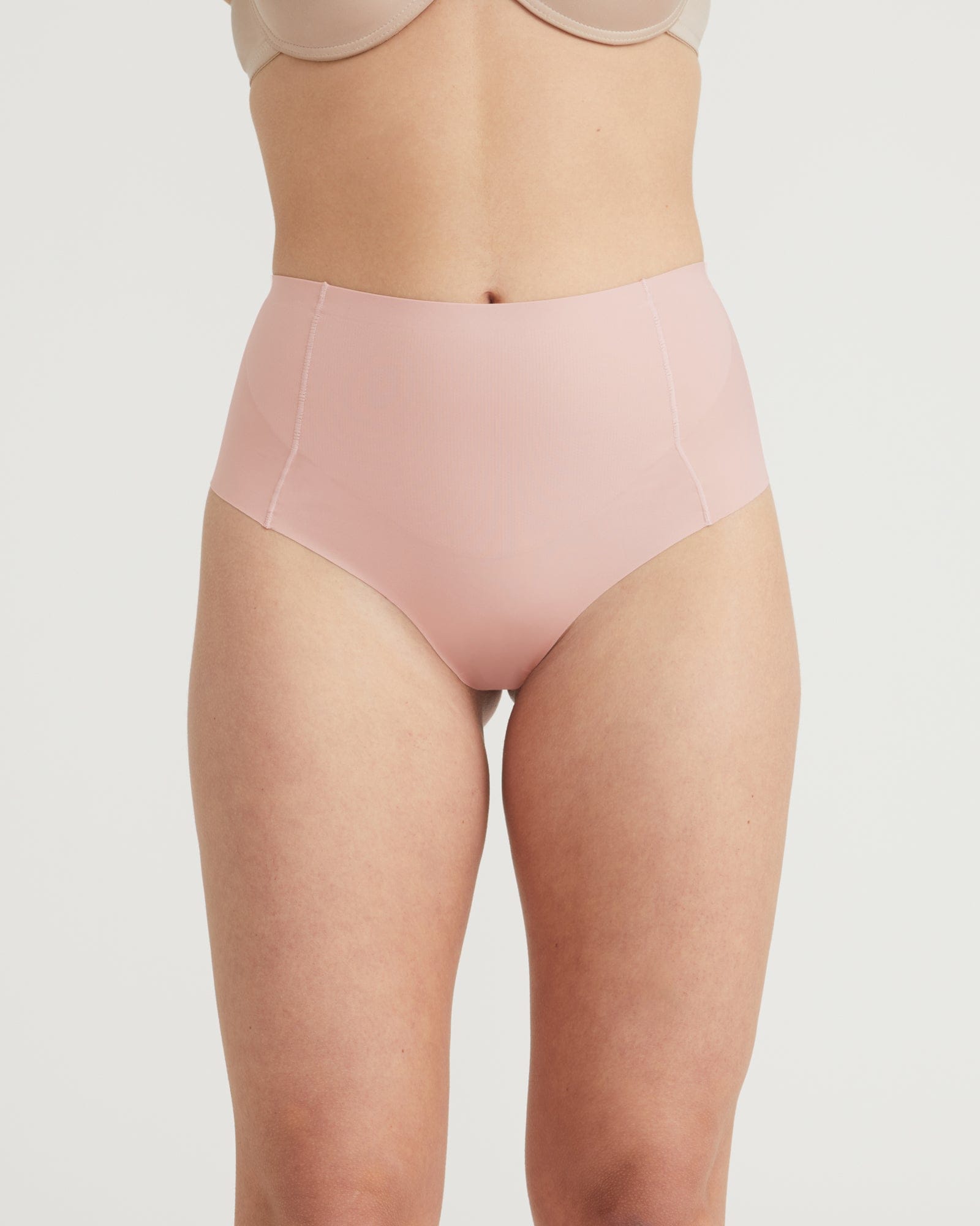 Person wearing a light pink high-waisted underwear on a plain background
