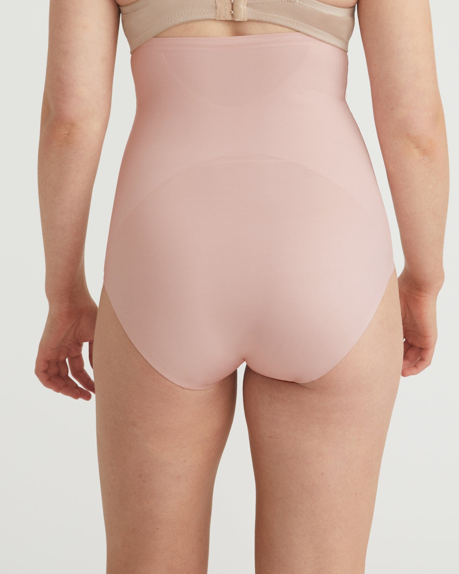 Person wearing a light pink high-waisted shapewear garment on a plain background