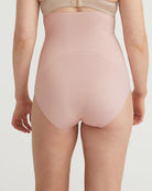 Person wearing a light pink high-waisted shapewear garment on a plain background