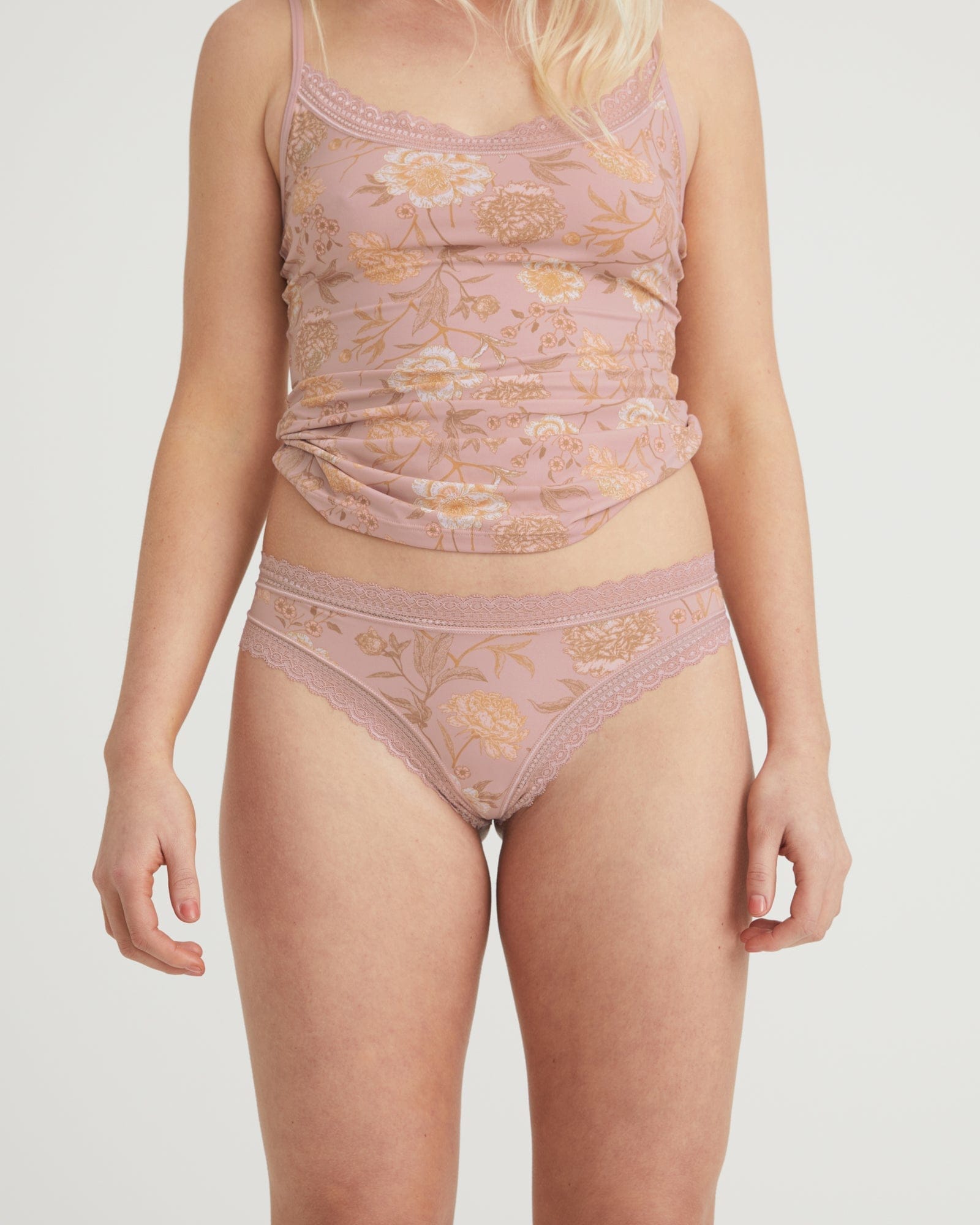 Woman wearing a matching pink floral lingerie set on a plain background