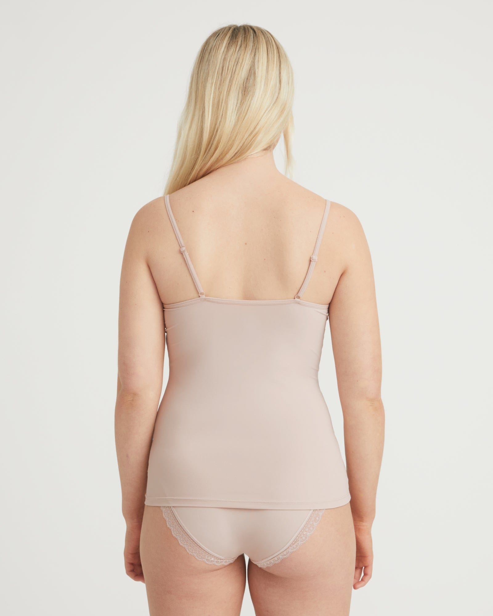 Woman wearing a beige tank top and underwear set on a plain background