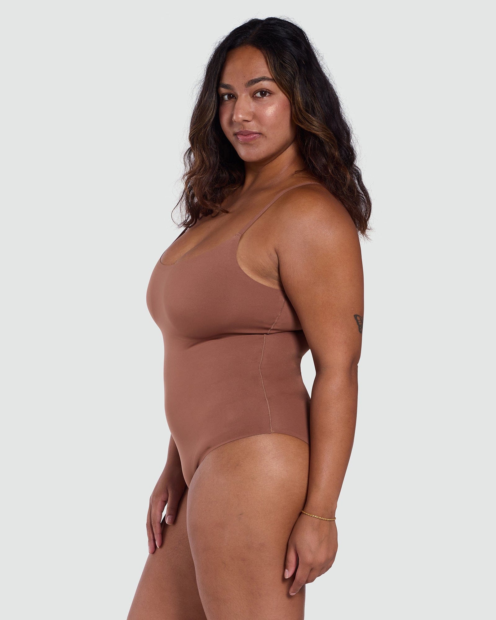 Woman wearing a brown bodysuit against a white background
