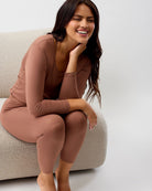 Woman wearing a brown outfit sitting on a beige chair against a white background