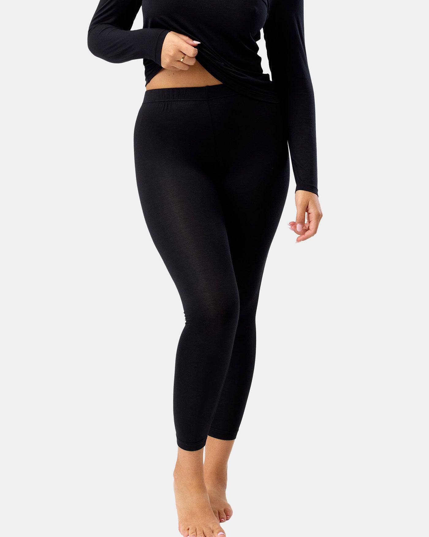Person wearing black leggings and a black long-sleeve top on a white background