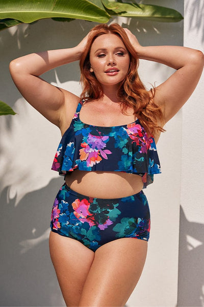 Model standing by pool wearing navy high waisted swim pant with floral print for curve women