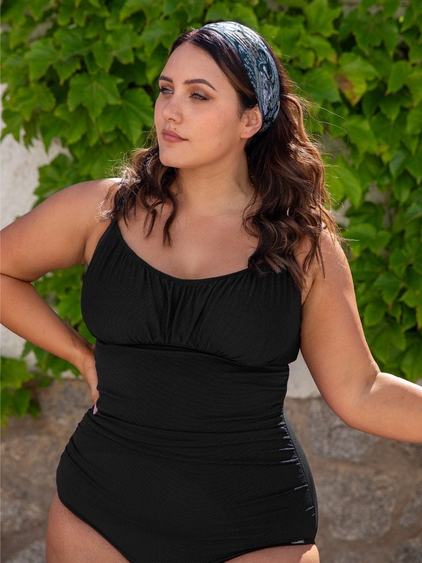 Woman wearing a black swimsuit with greenery in the background