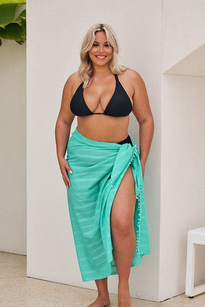 Blonde model wearing jade coloured sarong over black bikini