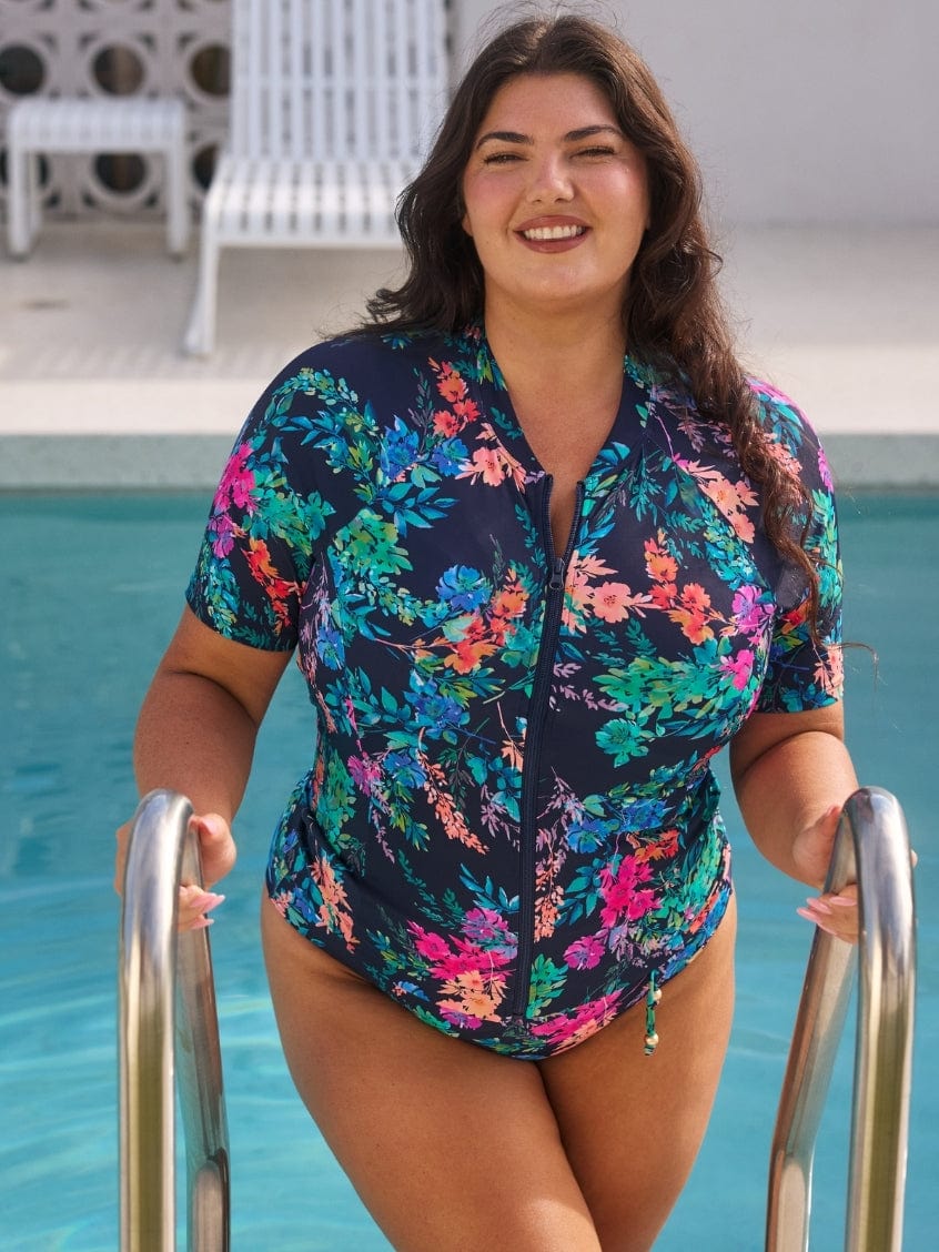 Woman in a floral rash vest swimsuit standing by a pool