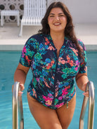 Woman in a floral rash vest swimsuit standing by a pool