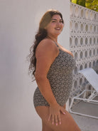 Woman wearing a patterned swimsuit standing outdoors against a white wall.