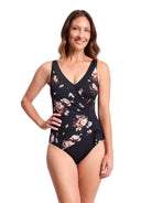 A woman modeling a one-piece swimsuit with a black base and a floral print in beige, white, and brown, set against a plain white background.