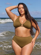 Woman in an olive green bikini standing on a beach with ocean waves in the background