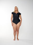 Person wearing a black swimsuit with cap sleeves on a white background