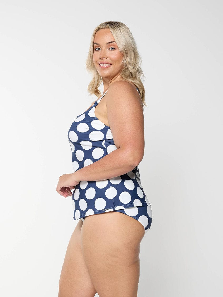Blonde model shows the side of high waisted tummy control swim bottom in navy and white dots pattern