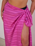 Pink striped sarong with pom-pom details on a plain background