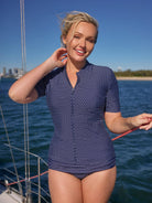 Woman in a blue patterned swimsuit on a boat with water and sky in the background