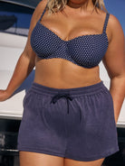 Woman wearing a navy polka dot bikini top and matching shorts with a blurred background.