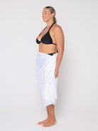 Woman wearing a black bikini top and white sarong on a plain background