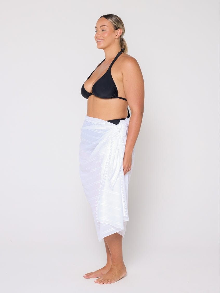 Woman wearing a black bikini top and white sarong on a plain background