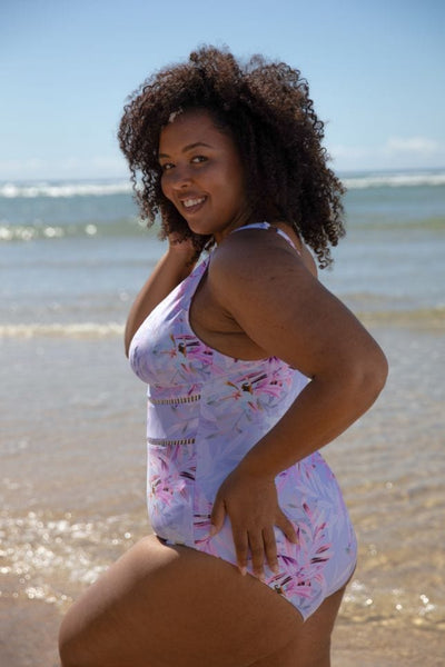 Brunette model wears lilac tropical floral one piece with low v neckline and lace trim