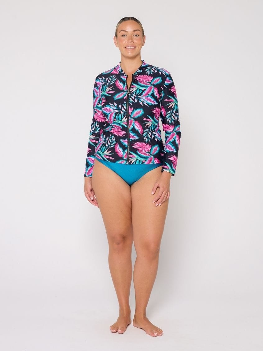 Woman wearing a colorful long-sleeve rash guard and blue swimsuit on a white background
