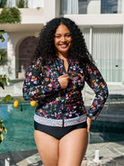 A woman wearing a floral long-sleeve swim jacket over a black bikini stands by a swimming pool in front of a modern white building.