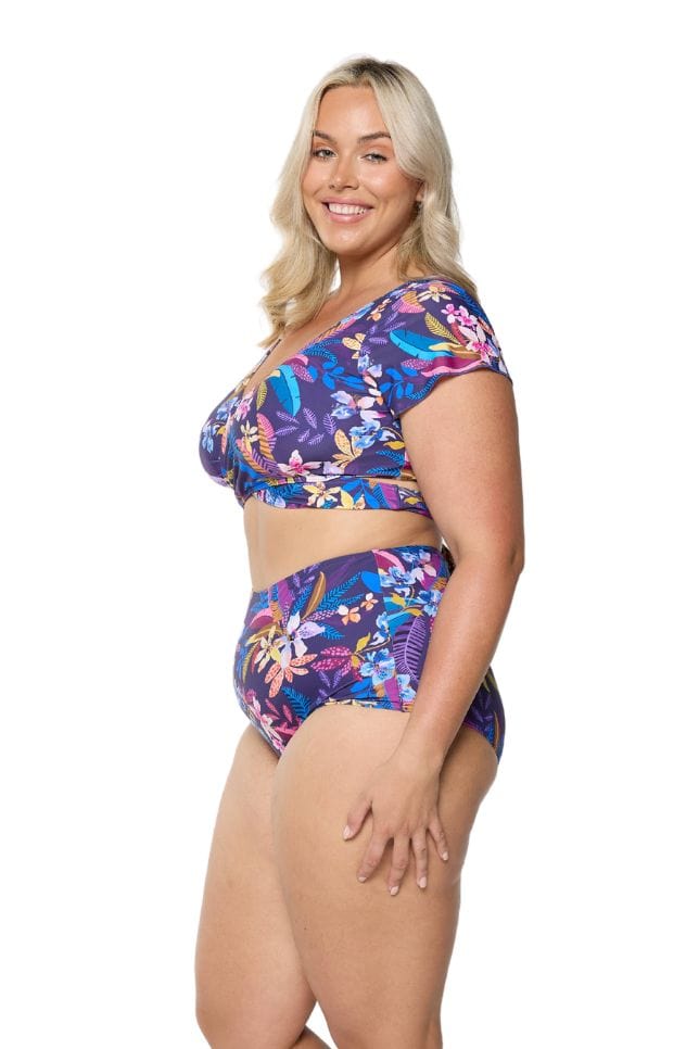 Side of model in studio wearing plus size swim pant in navy based floral tropical print