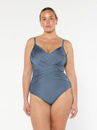 Blonde model in studio wearing a criss cross one piece with ruching and adjustable straps in metallic grey