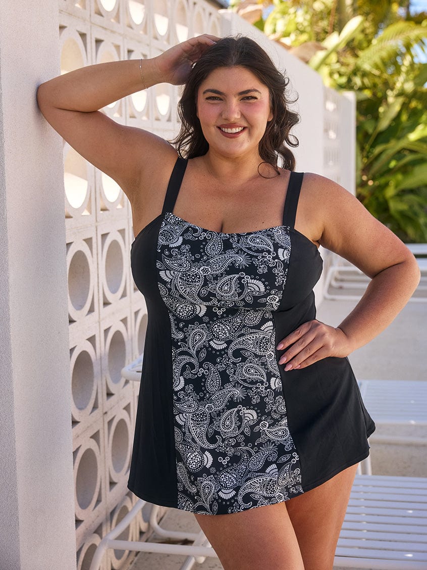 Brunette woman by pool wearing a chlorine resistant paisley swim dress with wide strap adjustable straps