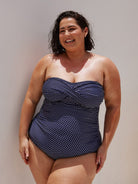 brunette model wearing a strapless one piece bathing suit with twist detail in between the breast area