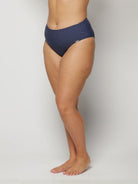 Woman wearing navy blue polka dot bikini bottom on a light gray background