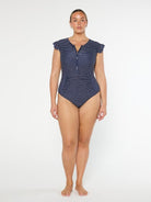 Woman wearing a navy polka dot swimsuit on a white background