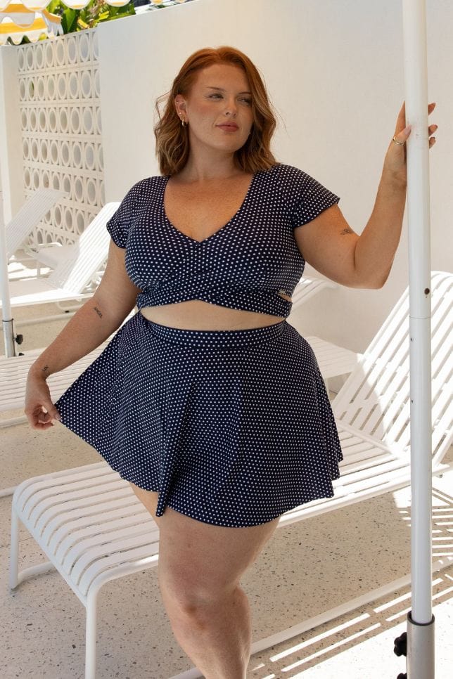 Plus size model standing by pool wearing skirt coverup in navy and white dot print