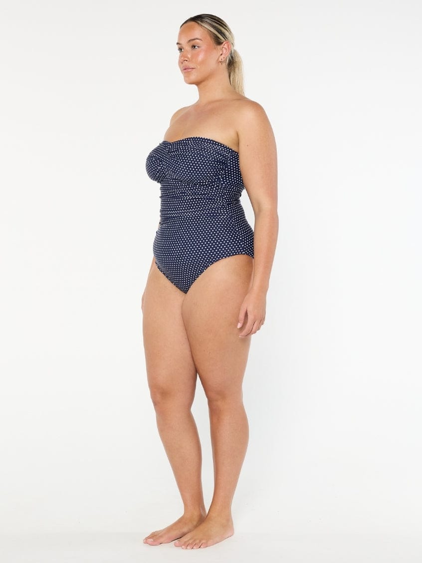 Woman wearing a navy polka dot strapless swimsuit on a white background