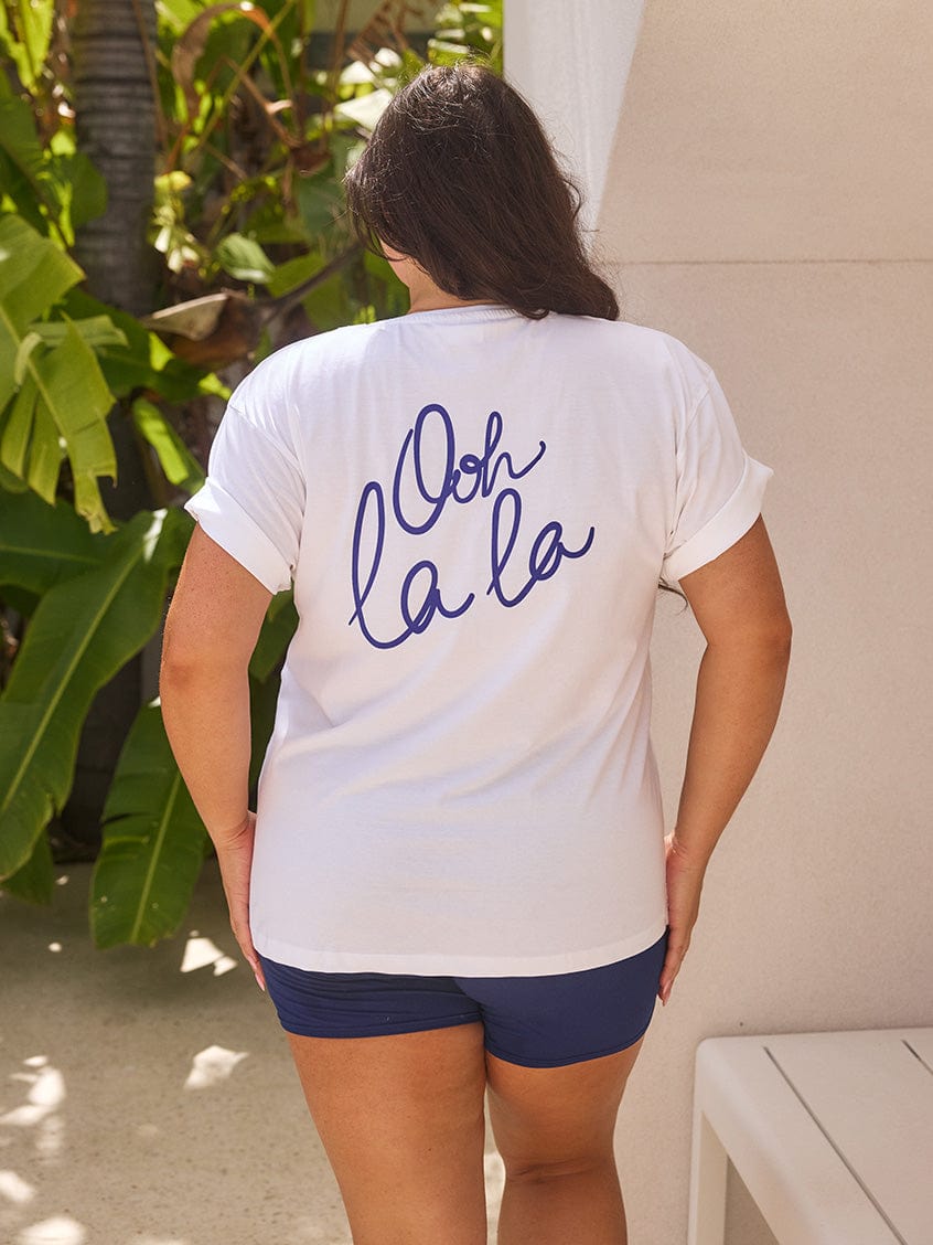 Person wearing a white t-shirt with 'Ooh la la' text in blue on the back, standing outdoors.