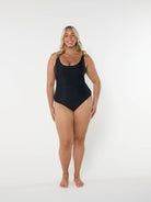 Women wearing a black one piece swimsuit standing in front of a white wall