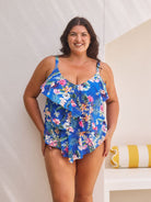 Brunette model wears tummy control tankini top with shelf bra in blue floral print