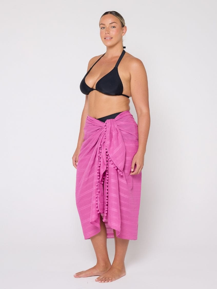 Woman wearing a black bikini top and pink sarong on a white background