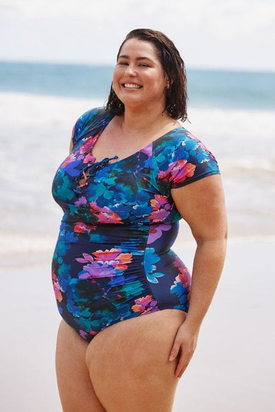 Side profile of model on beach wearing navy floral one piece with cap sleeves and tie front detail for curvy women