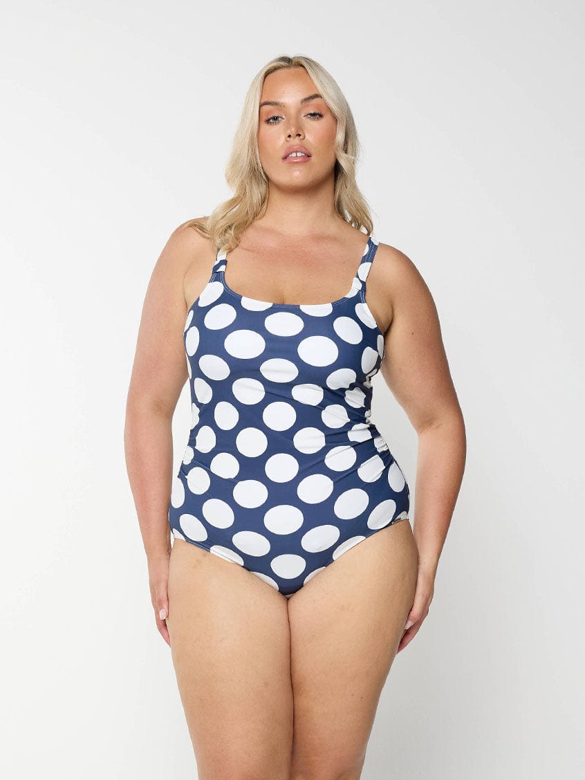 Blonde woman showing the front of navy scoop neck one piece with large white polkadots