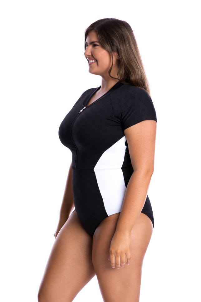 Brunette model wearing a plus size black and white zip up one piece swimsuit