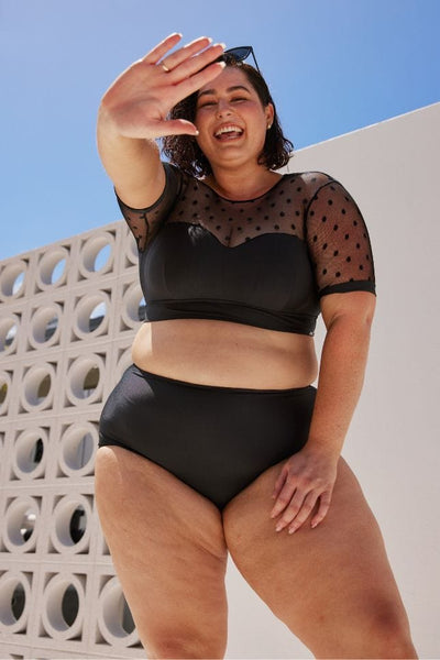 brunette model wearing a retro styled black crop bikini top with mesh polkadots on the sleeves 