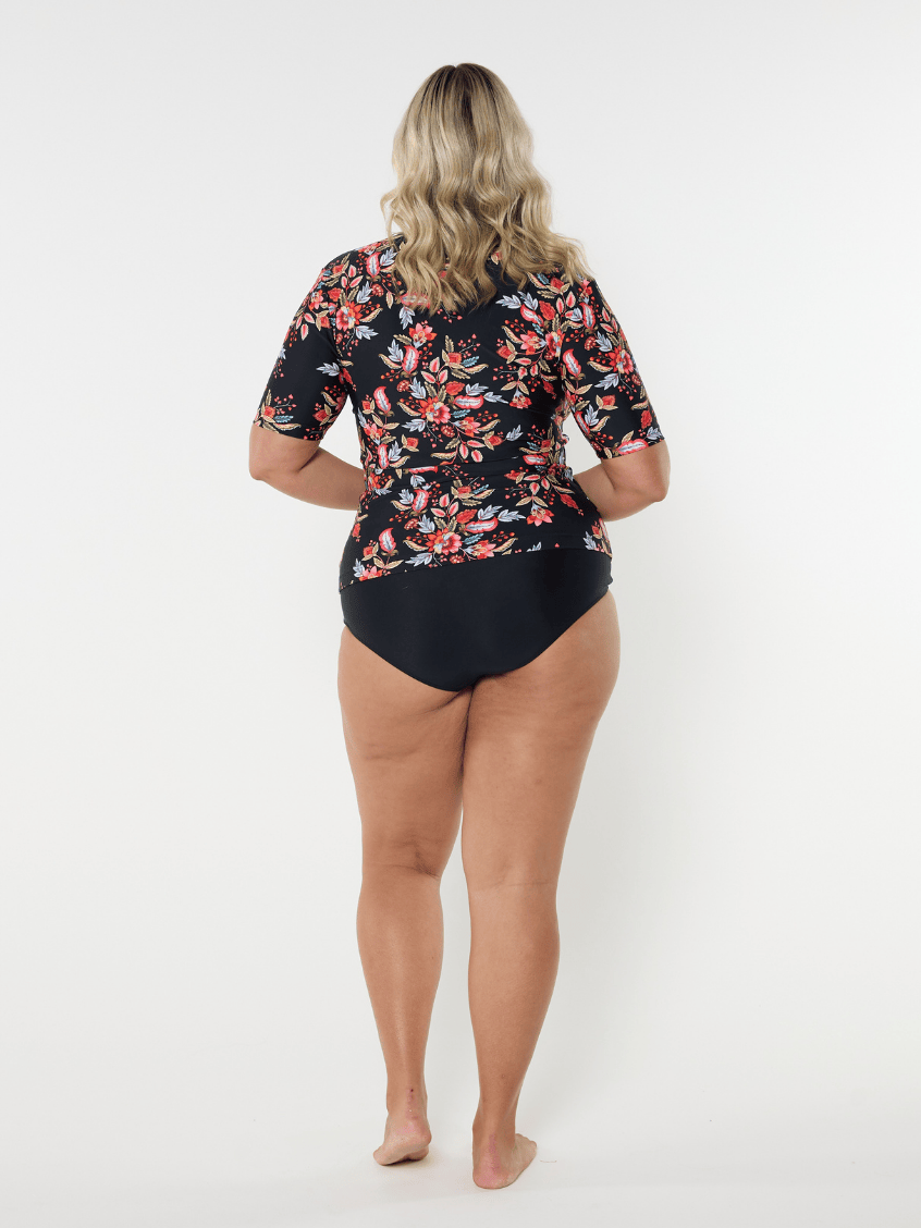 Woman wearing a floral rash guard and black swimsuit bottoms on a white background