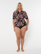 Woman wearing a floral rash guard and black bottoms on a white background