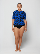Person wearing a blue patterned rash guard and black shorts on a white background