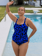 Woman in a chlorine resistant blue and black patterned swimsuit standing by a pool.